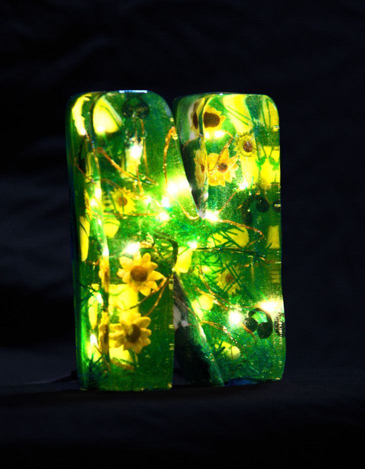 An 'N' made of epoxy resin. Inside, some fairy lights glow and sunflowers, headphones, earplugs and artificial grass float around. The letter is coloured deep green.
        Photo (c) c3awareness | TRim